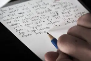 Eine Hand, die einen Bleistift hält und damit einen Text auf ein Blatt Papier schreibt